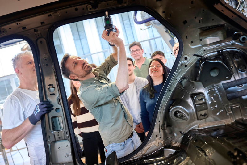 A worker explains an assembly step on the body of the VW ID.3 to the guests