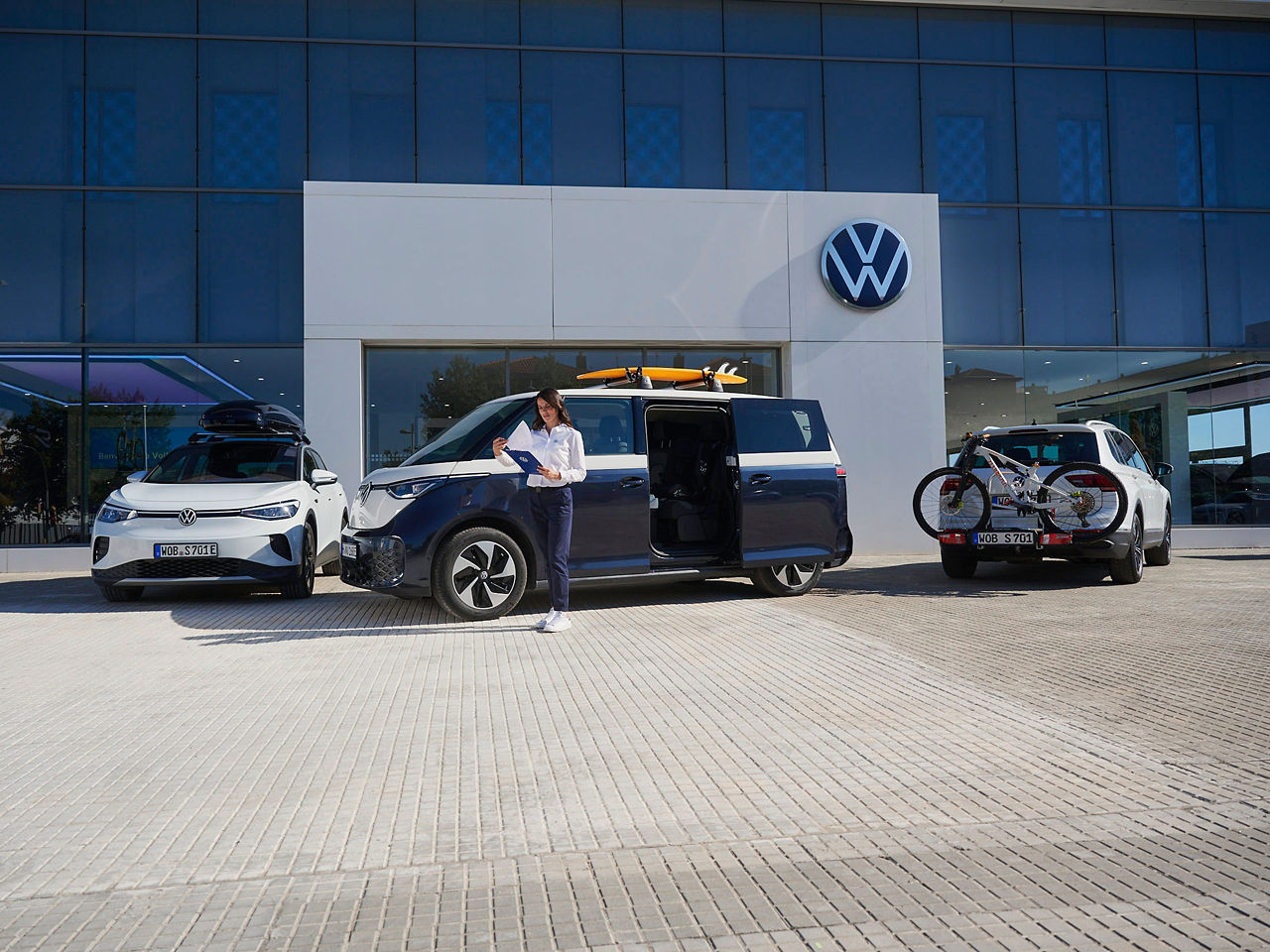 VW Servicemitarbeiterin mit Klemmbrett in der Hand steht vor VW ID. Buzz, daneben VW ID.4 und VW Tiguan