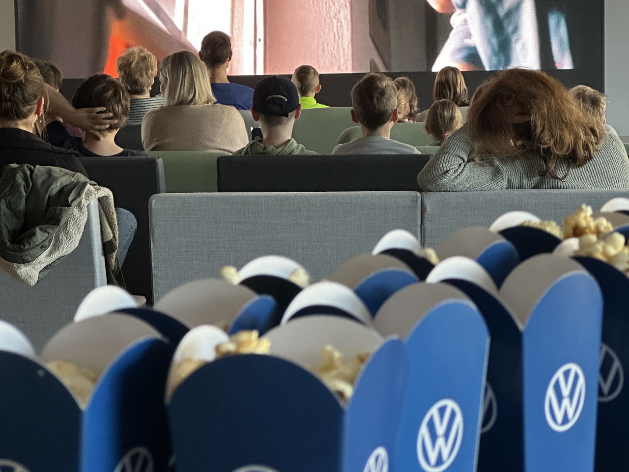 Popcorn un einer VW Tüte, im Hintergrund sind Personen die auf eine Leinwand blicken
