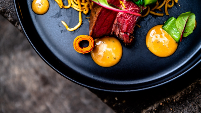 Es ist nur eine hälfte eines schwarzen Tellers im Bild zu sehen. Darauf eine Variation aus Fleisch und Salat.