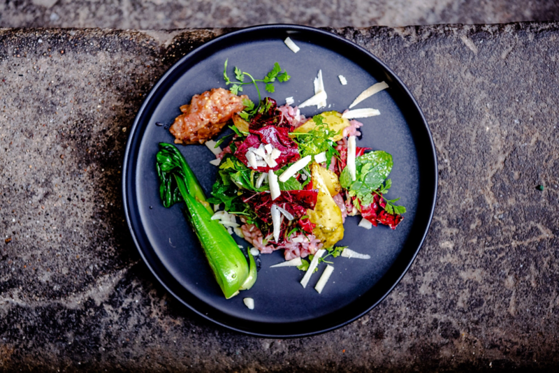 Ein schwarzer Teller steht auf einer dunklen Steinplatte. Auf dem Teller ist ein Salat trapiert.