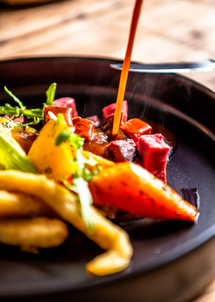 Eine Variation aus Rinderragout und Beilage auf einem schwarzen Teller.